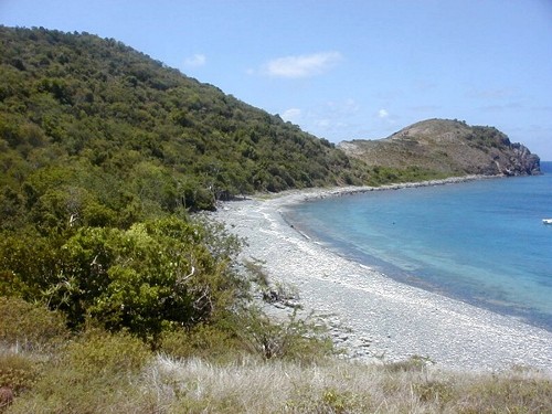 Ocean waves crashing on a pebble beach in front of vegetation-covered hills